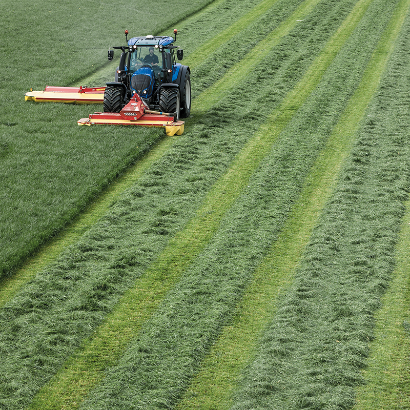 Blauer Valtra-Traktor mit Mähwerk auf Wiese